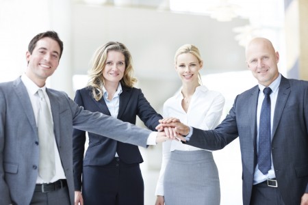 Four executives with hands touching in the middle, smiling at the camera - copyspace